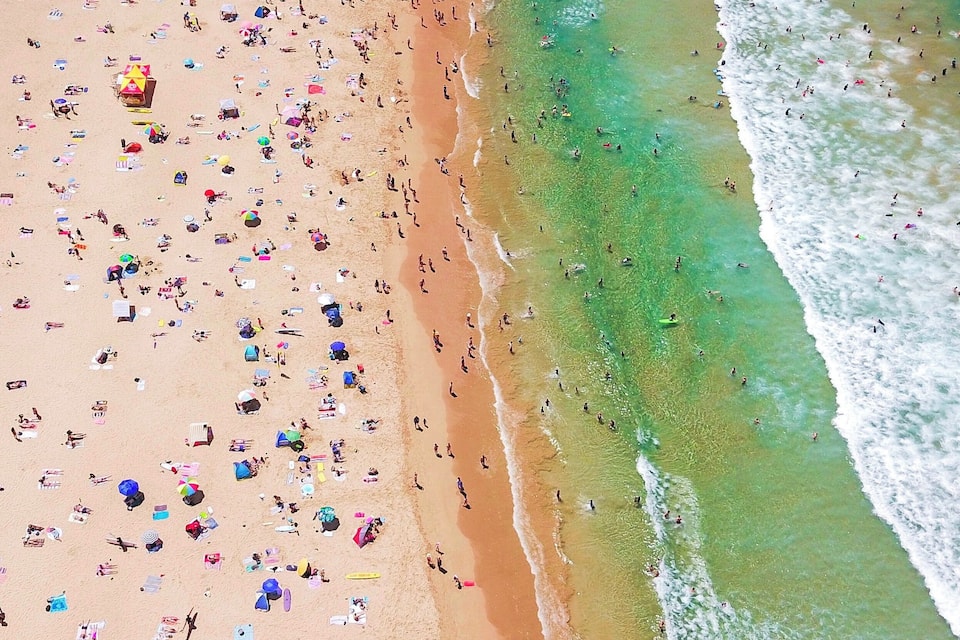 Luftaufnahme eines überfüllten Strandes mit zahlreichen Sonnenschirmen und Menschen, die das Ufer genießen.