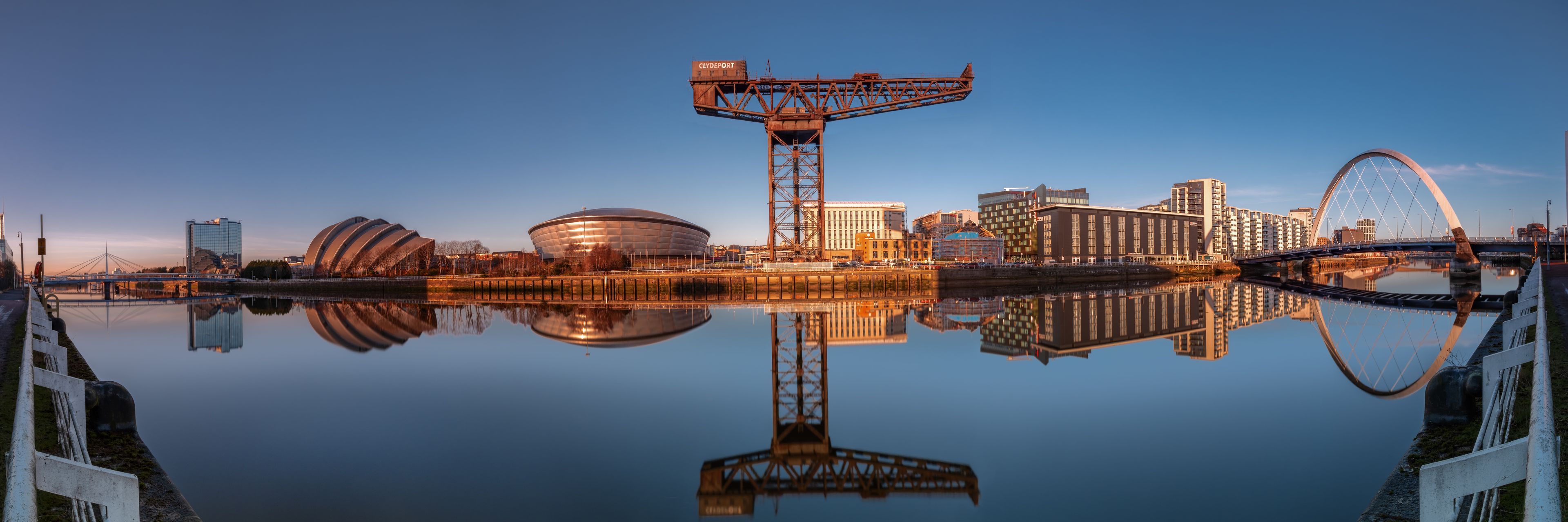 A waterfront cityscape with a large circular building, a bridge, and a Ferris wheel.