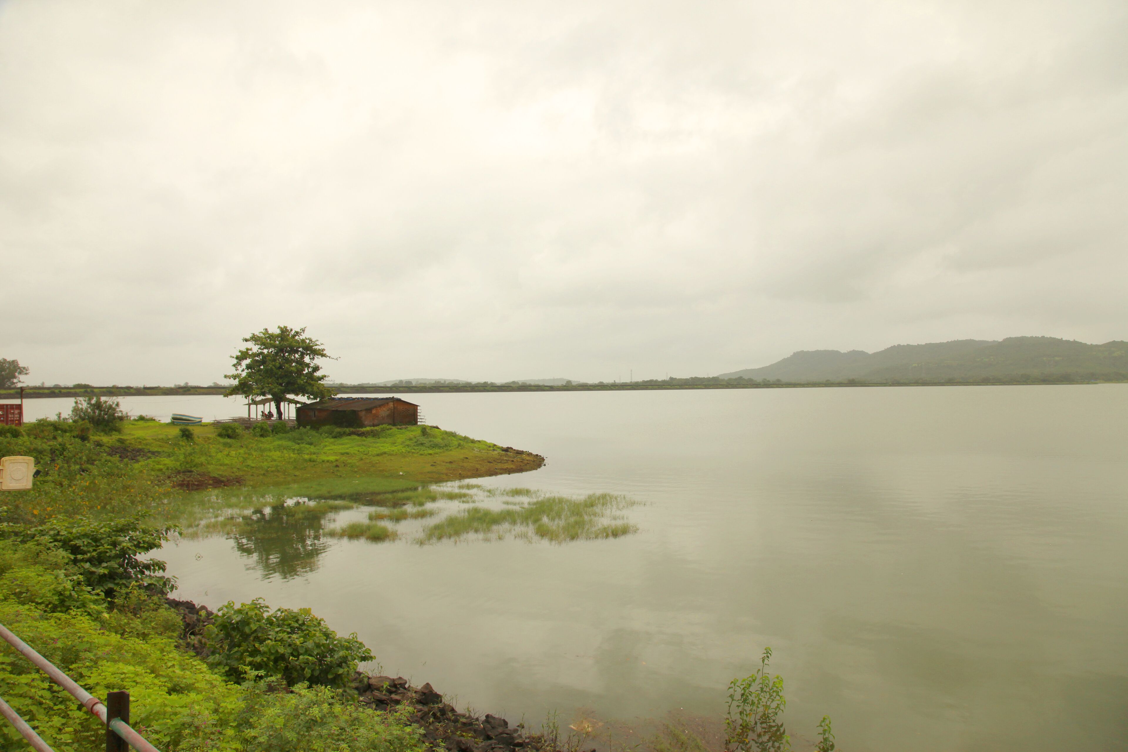 A calm lake with a small island, a tree, and a distant mountain range under a cloudy sky.