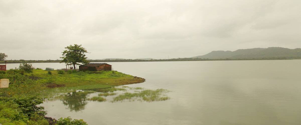 A calm lake with a small island, a tree, and a distant mountain range under a cloudy sky.