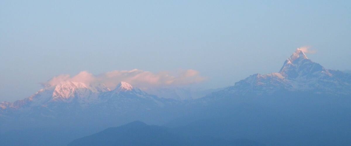 A mountain range with snow-capped peaks and a hazy sky.