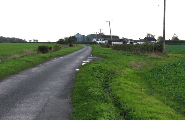 Road past Priory Farm Priory Farm is in the distance on the edge of the square.