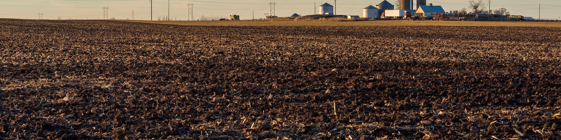 A winter farm field with distant silos and farm buildings