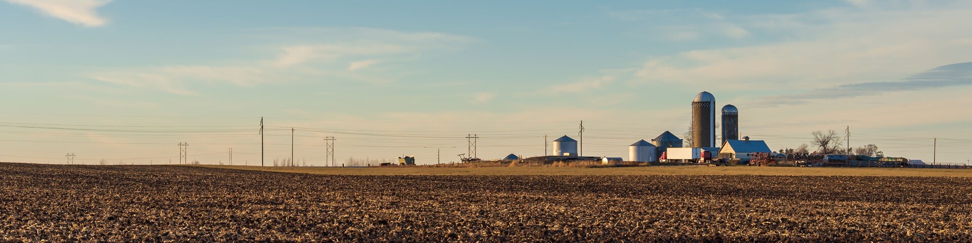 A winter farm field with distant silos and farm buildings