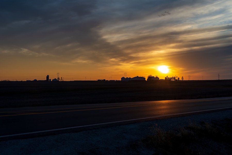 Un atardecer sobre una llanura con una carretera y edificios a lo lejos.