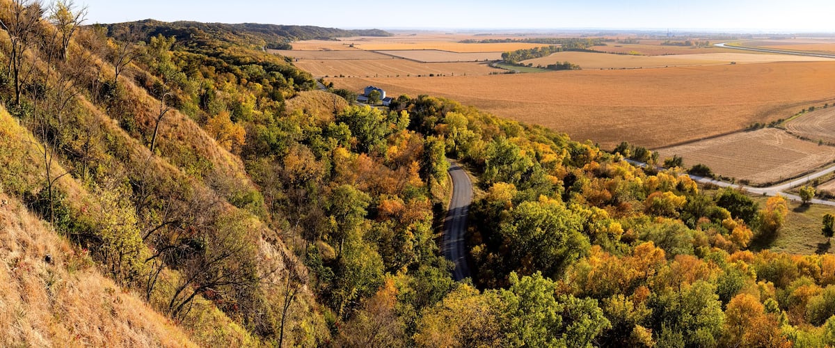 A hilly landscape with autumn foliage, a winding road, and expansive fields.