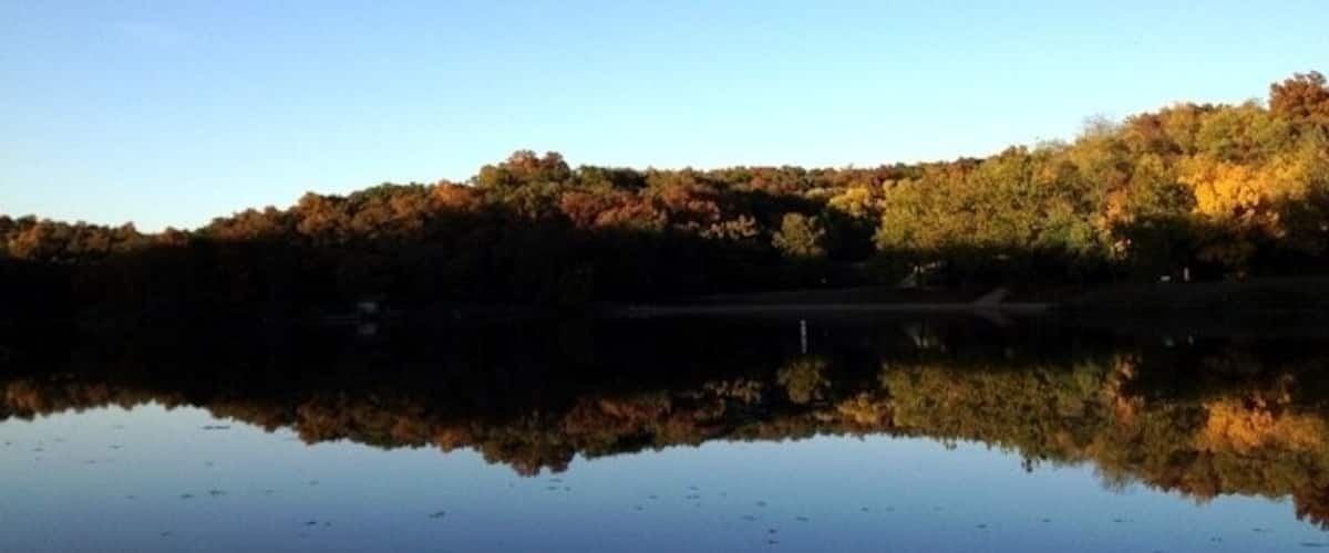 A calm lake reflecting trees with autumn foliage.