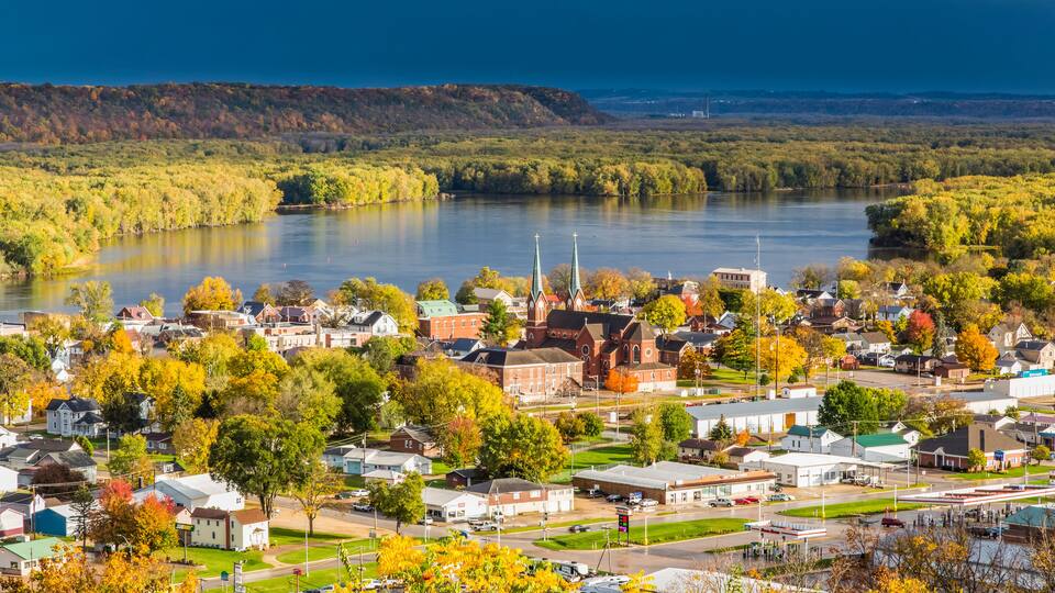 A riverside town with a prominent church, a bridge, and surrounding greenery.