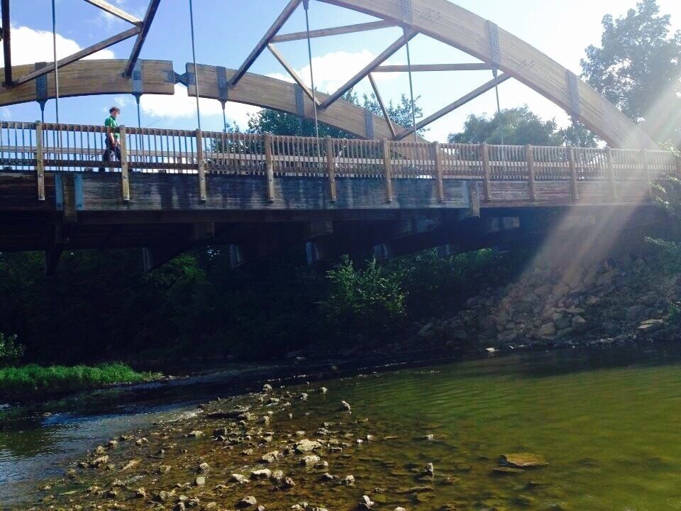 A wooden pedestrian bridge over a river with a person standing on it.