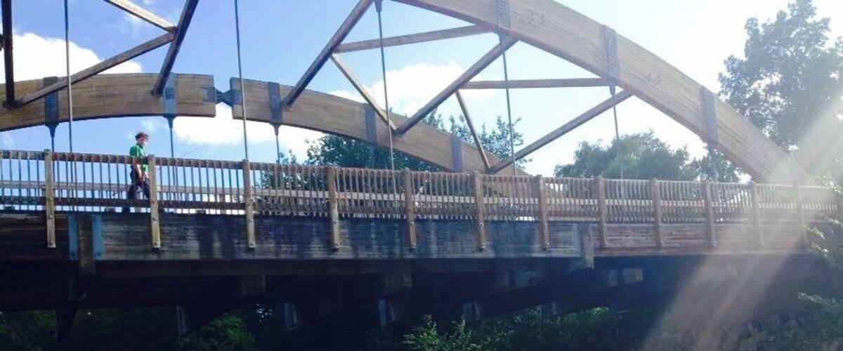 A wooden pedestrian bridge over a river with a person standing on it.