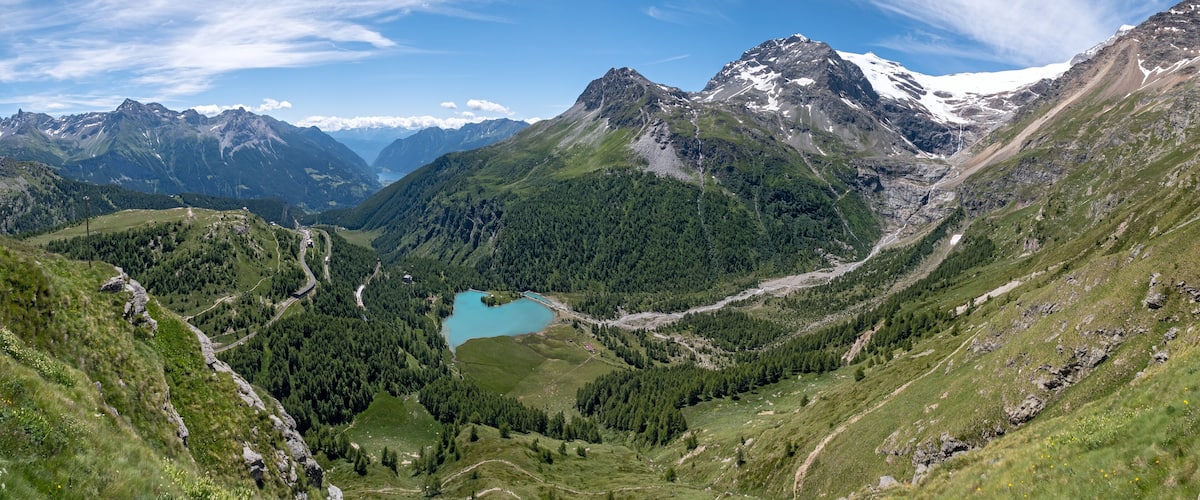 A mountainous landscape with a turquoise lake, green valleys, and snow-capped peaks.