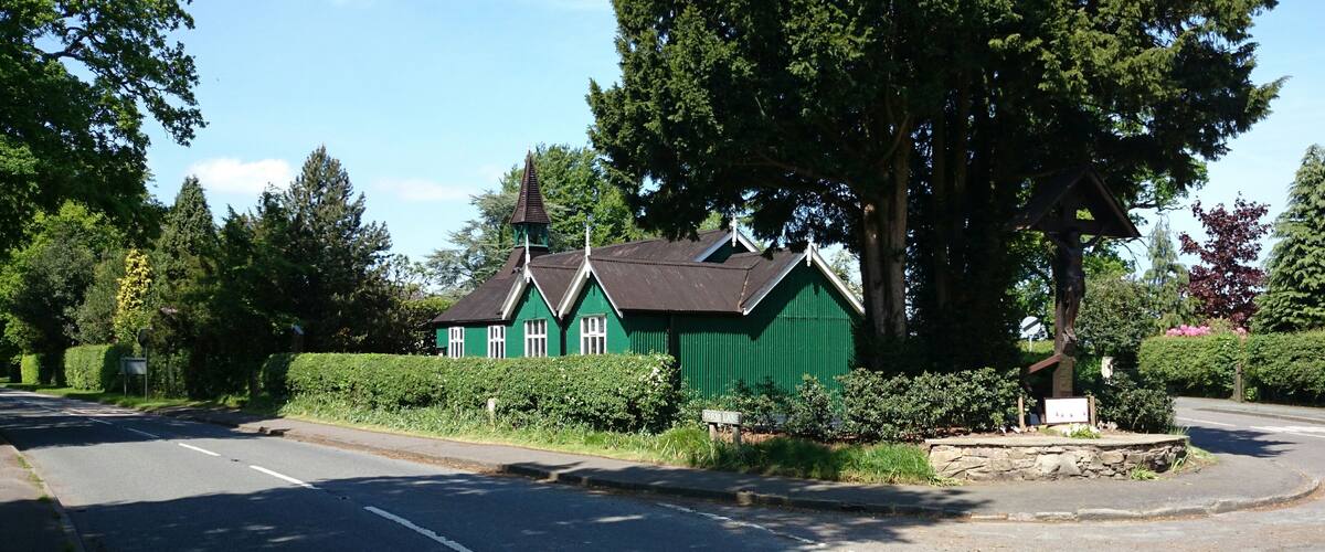 A green building with a pointed roof, surrounded by trees and a hedge.