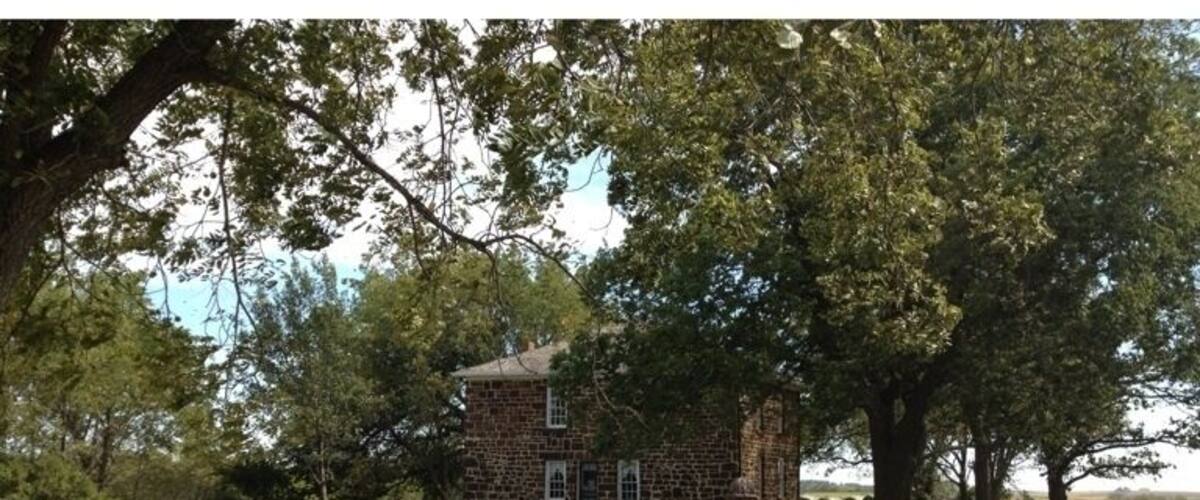 A stone sign with "Hitchcock House Underground Railroad Station" written on it, surrounded by trees and a grassy area.