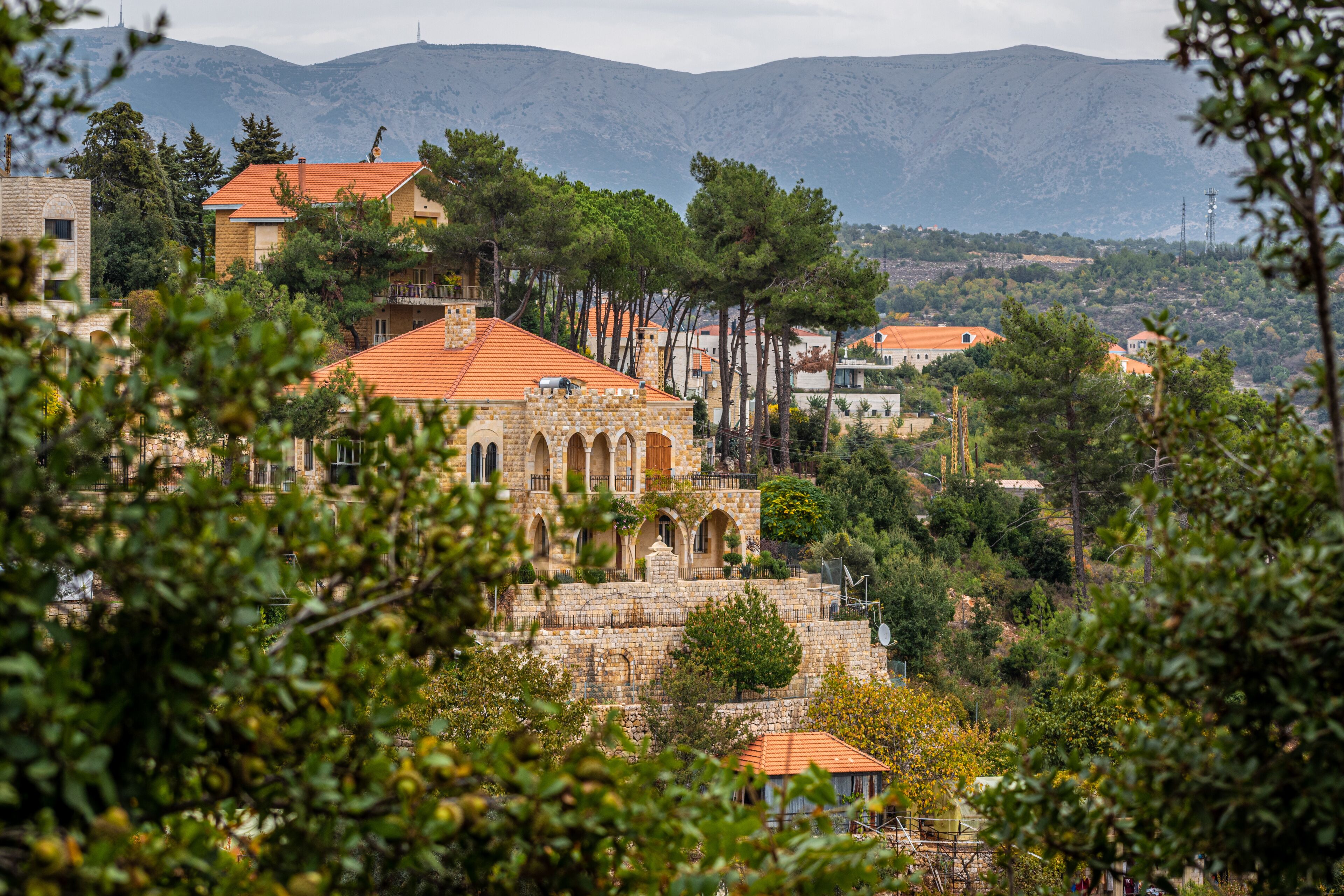A stone building with a red roof, surrounded by trees and hills in the background.