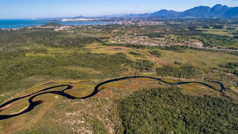 An aerial view of a coastal city with a river winding through the landscape, surrounded by mountains and dense forests.