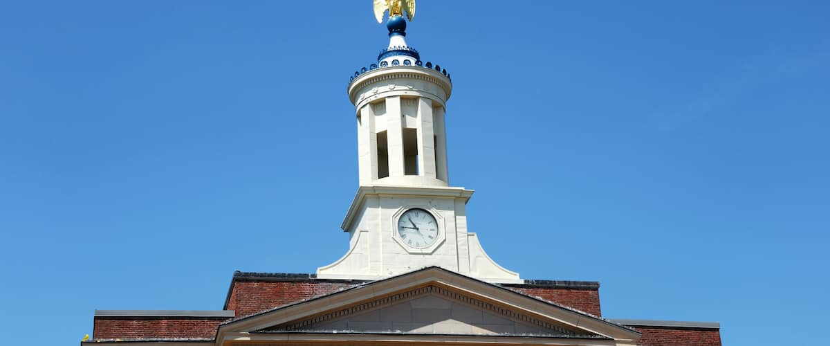A clock tower with a golden eagle statue on top, surrounded by clear blue sky.