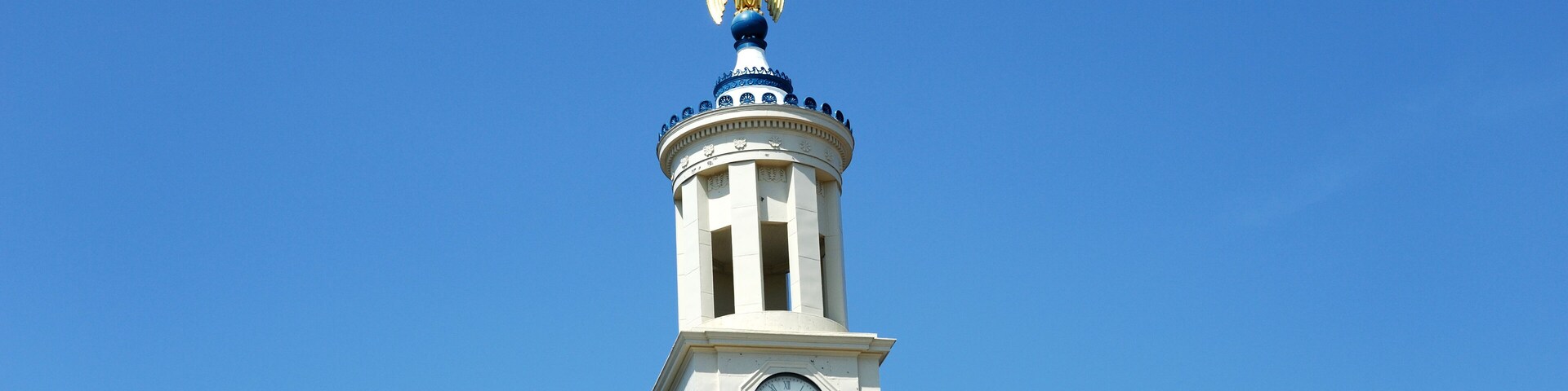 A clock tower with a golden eagle statue on top, surrounded by clear blue sky.