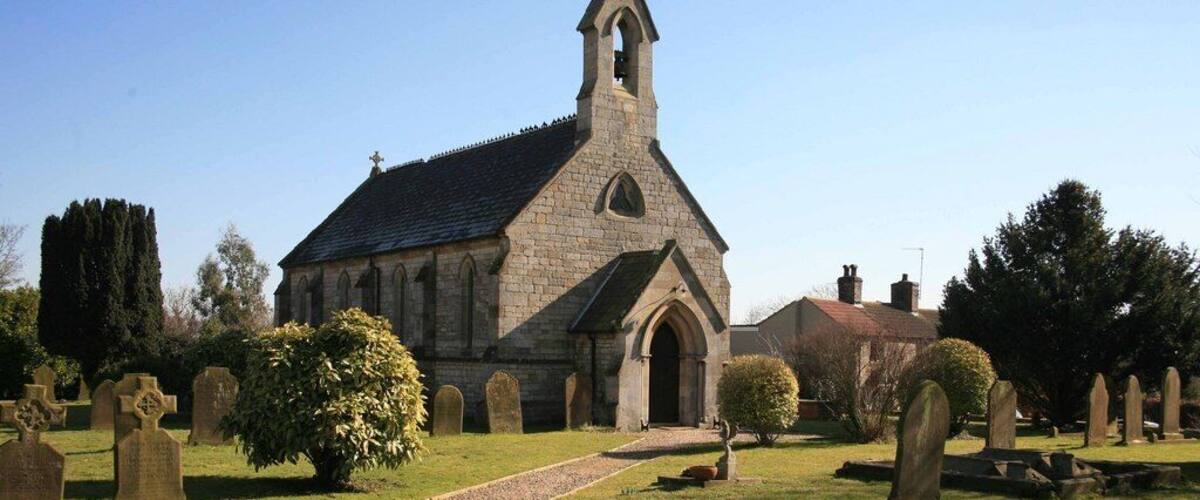 A church with a tall steeple, surrounded by a cemetery with headstones.