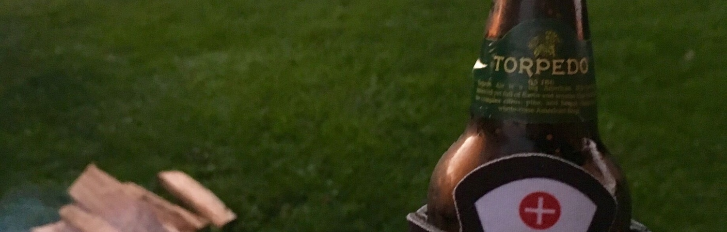 A hand holding a bottle of 'Courses Rock' beer with a tent and a campfire in the background.