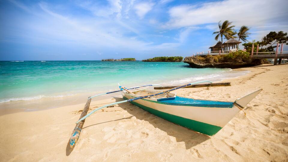 A beach with a boat, clear turquoise water, and a small hut on a rocky outcrop.