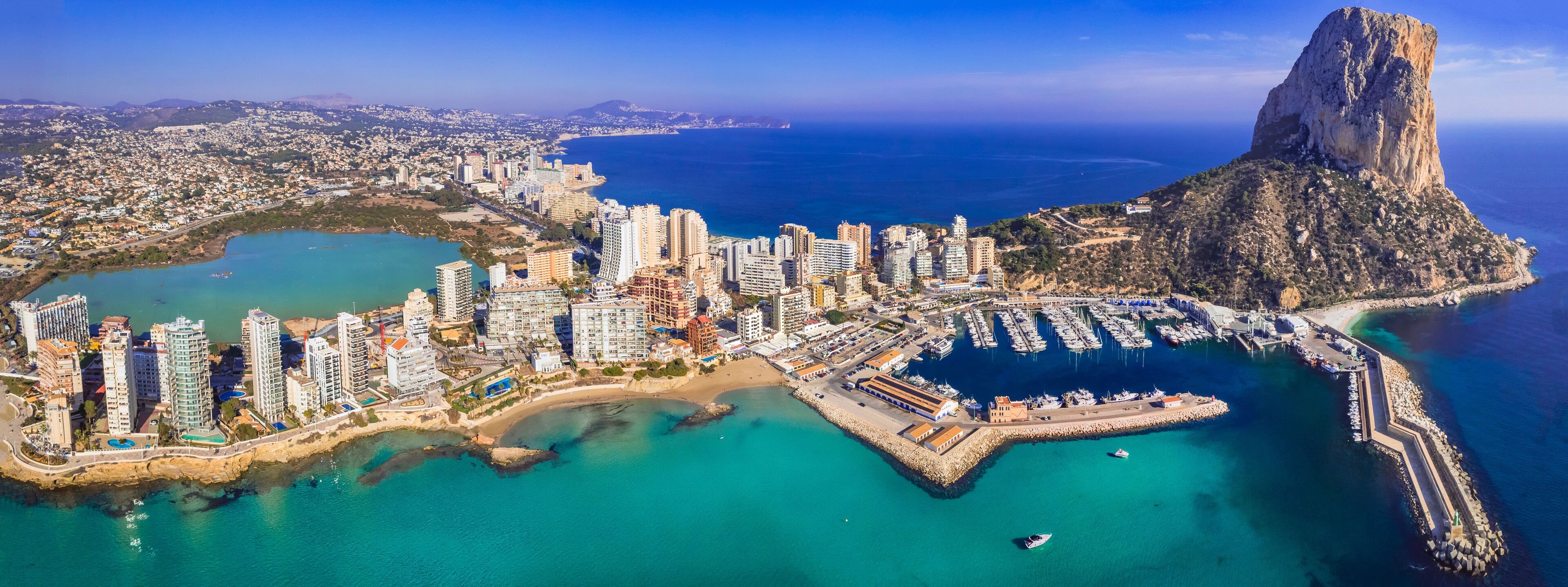 A coastal cityscape with high-rise buildings, a marina, and a prominent rocky cliff.