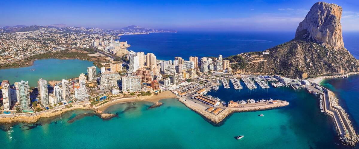 A coastal cityscape with high-rise buildings, a marina, and a prominent rocky cliff.