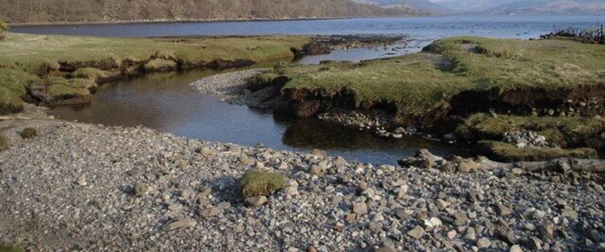 A calm lake with rocky shores and distant mountains.