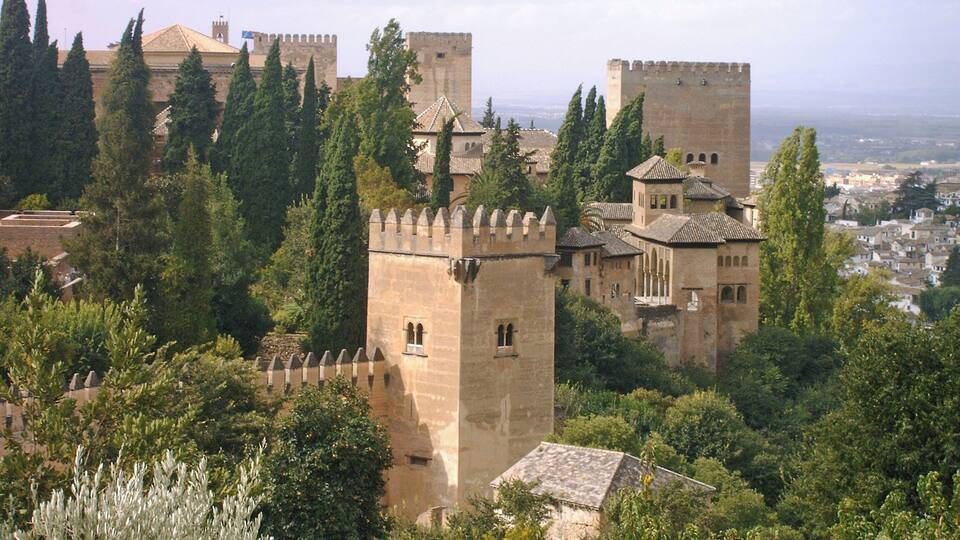 A historic castle surrounded by lush greenery and a distant cityscape.