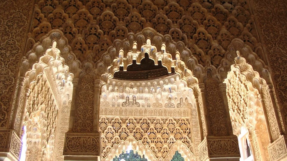 An intricately carved archway with detailed geometric and floral patterns, surrounded by ornate columns and a richly decorated ceiling.