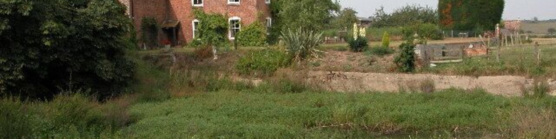 A rural landscape with a red brick house, a large tree, and a field.