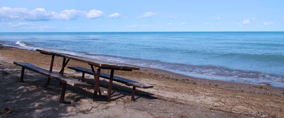 A beach with a wooden picnic table and a clear blue sky.