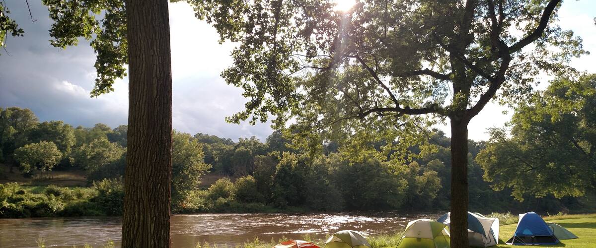 A river with tents and a picnic table in a grassy area.
