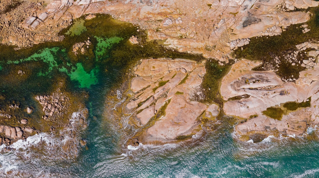Aerial panorama view of water flowing around large granite ledges covered in lichen and weed