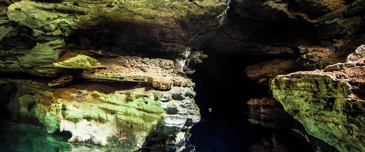 A cave with greenish rock formations and a clear water pool at the bottom.