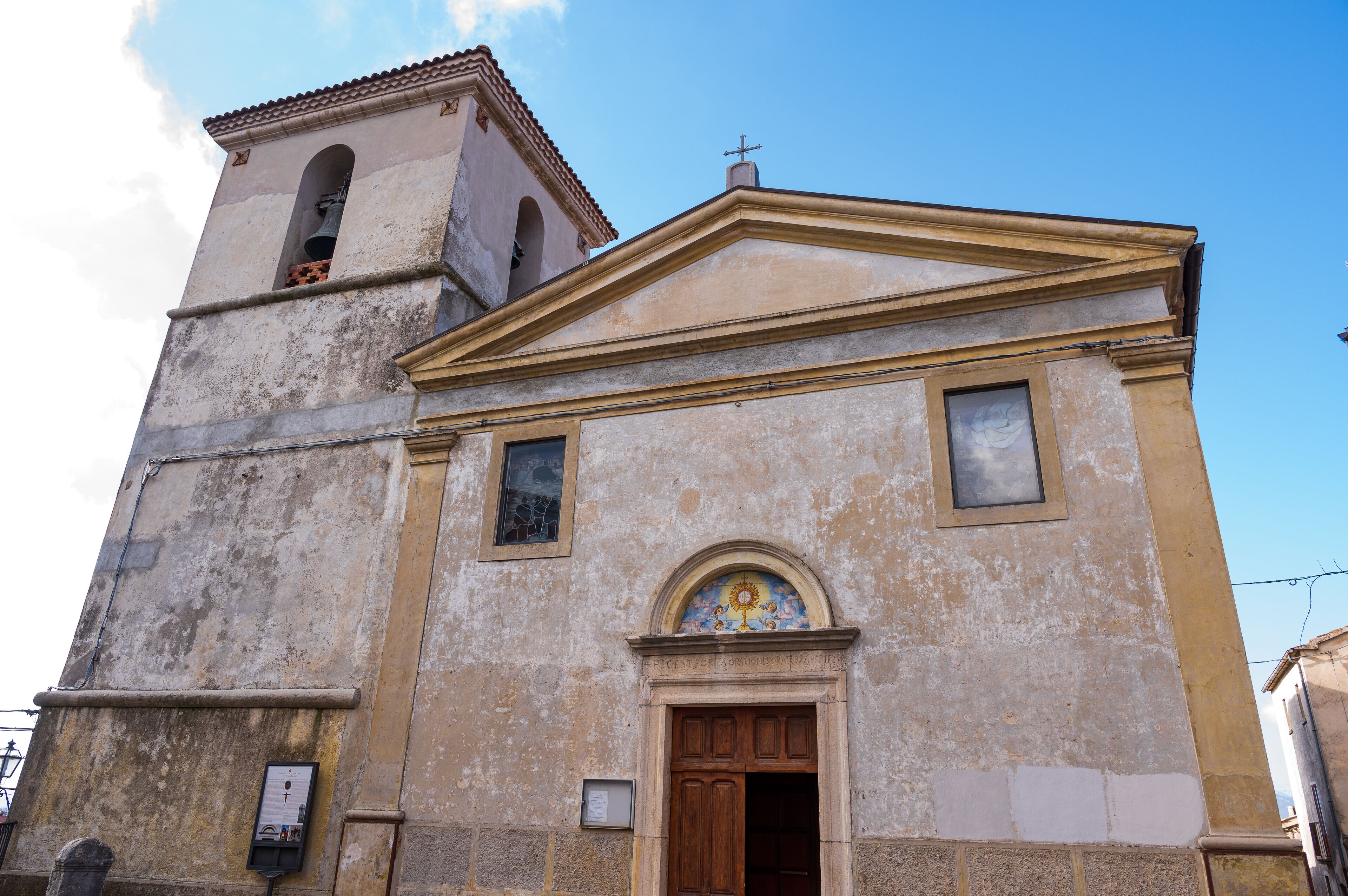 A weathered church with a bell tower and a large arched window with a sun motif.