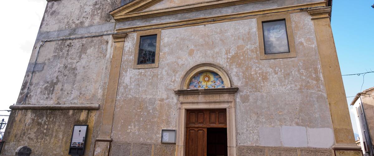 A weathered church with a bell tower and a large arched window with a sun motif.