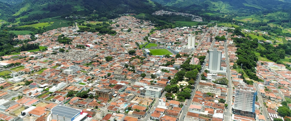 A city with red-roofed buildings, a central plaza, and green hills in the background.