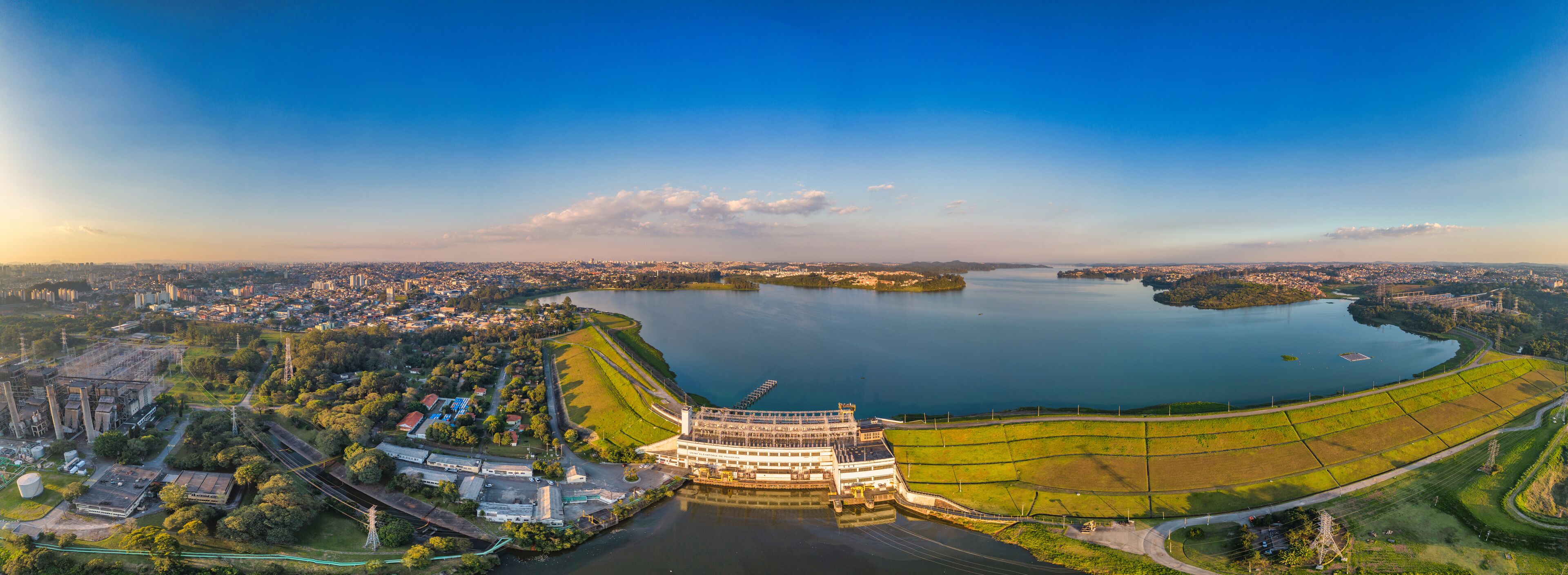A panoramic view of a city with a large body of water, a prominent building complex, and surrounding greenery.