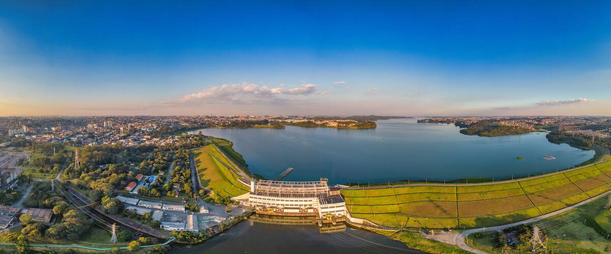 A panoramic view of a city with a large body of water, a prominent building complex, and surrounding greenery.