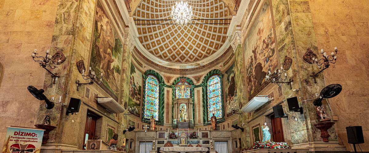 An ornate church interior with a high ceiling, stained glass windows, and a central altar.