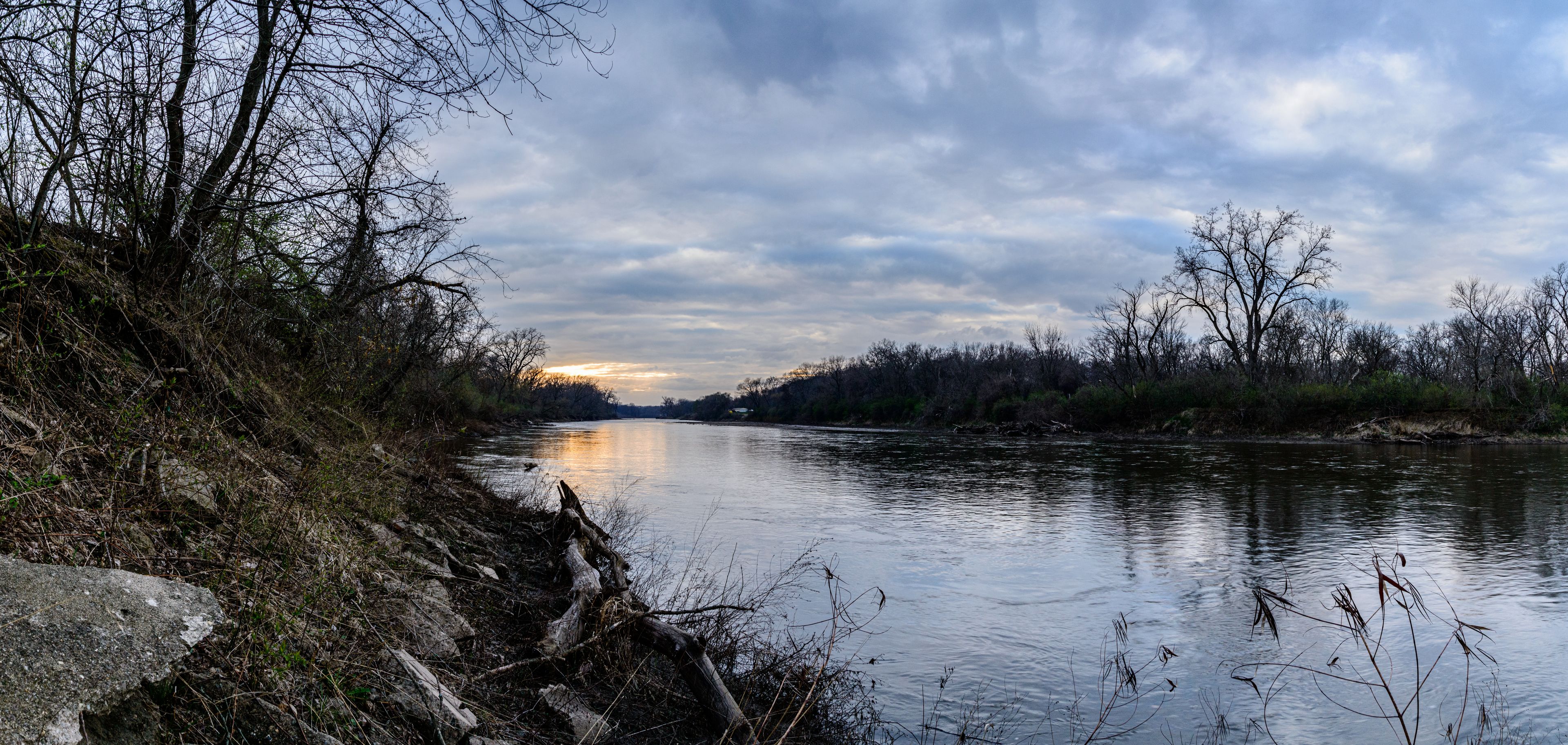 A river with a rocky bank and leafless trees under a cloudy sky.