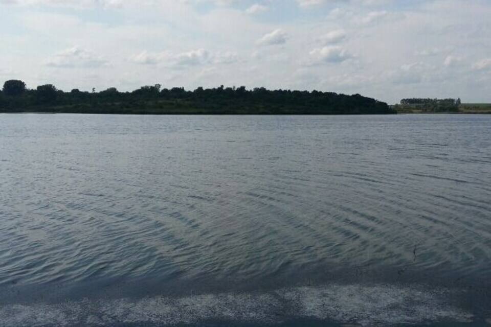 A calm lake with a rocky shoreline and a distant tree-covered island.