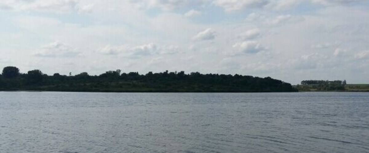 A calm lake with a rocky shoreline and a distant tree-covered island.