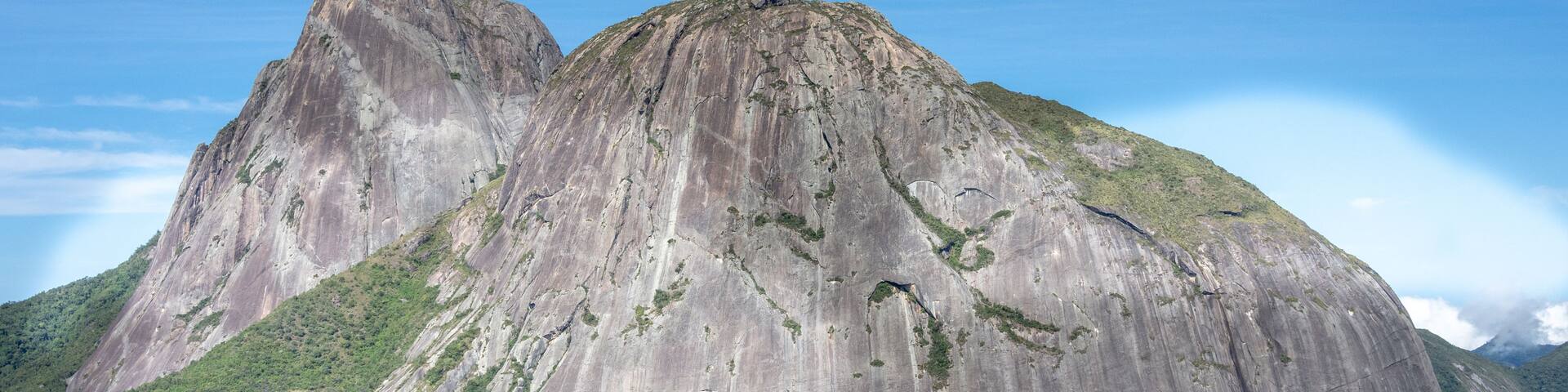 A large, rugged mountain with steep cliffs and a dense green forest at its base.