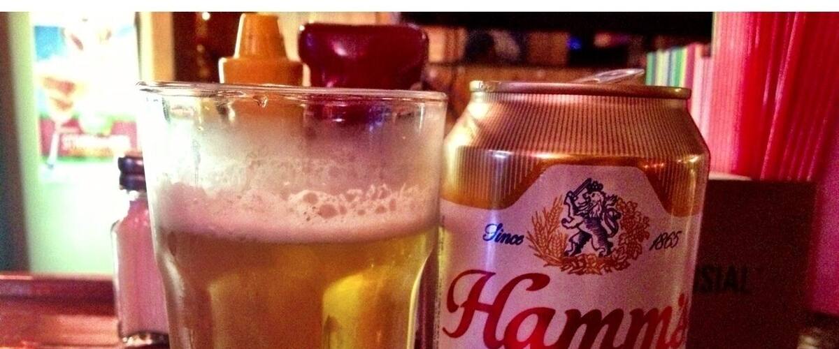 A glass of beer and a can of Hamm's beer on a wooden table.