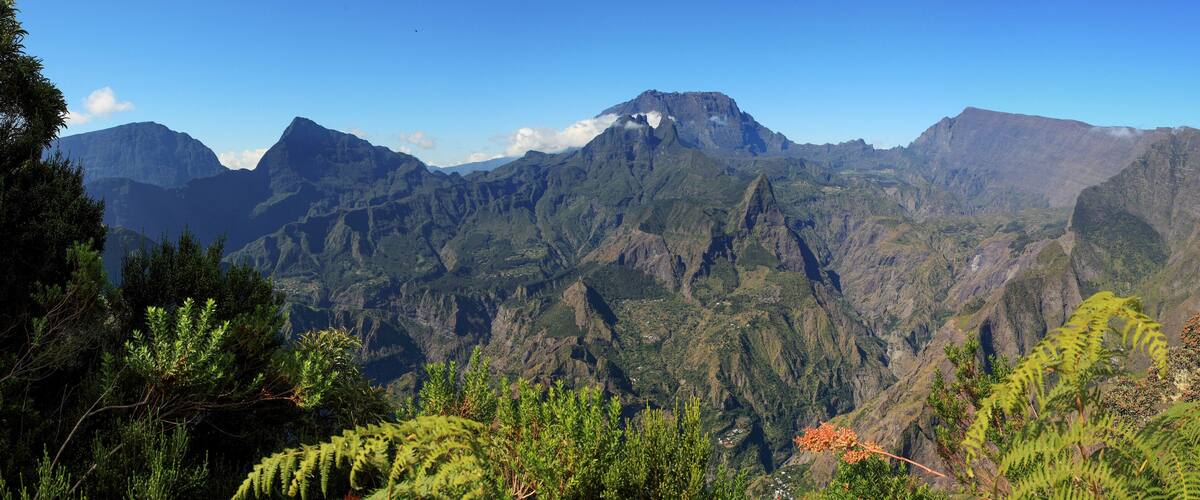A mountainous landscape with dense green forests and rugged peaks under a clear blue sky.