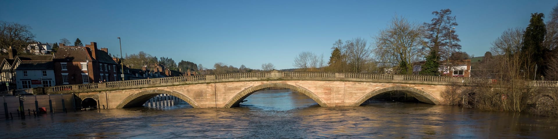 A stone bridge over a river with buildings on the left and trees on the right.