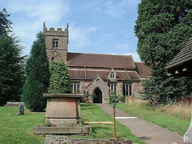 A church with a tower and arched entrance, surrounded by greenery and a pathway.