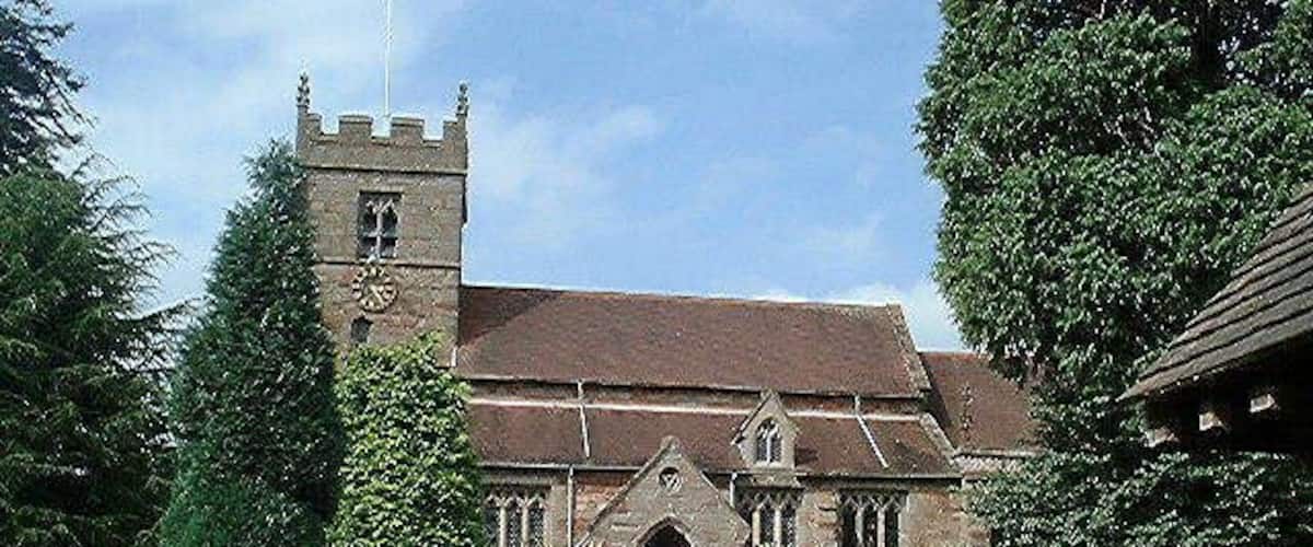 A church with a tower and arched entrance, surrounded by greenery and a pathway.