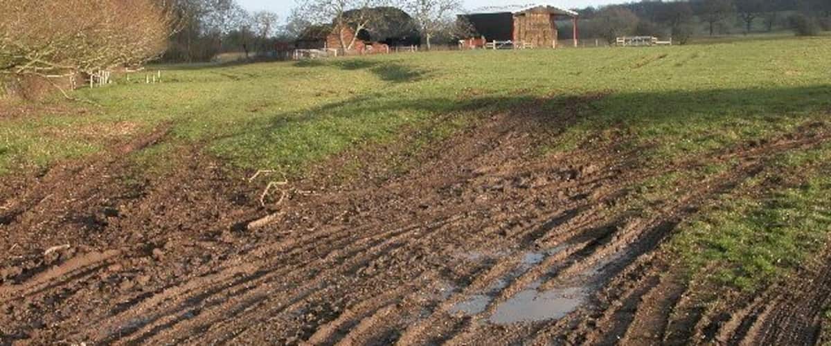 A muddy field with a barn in the background.